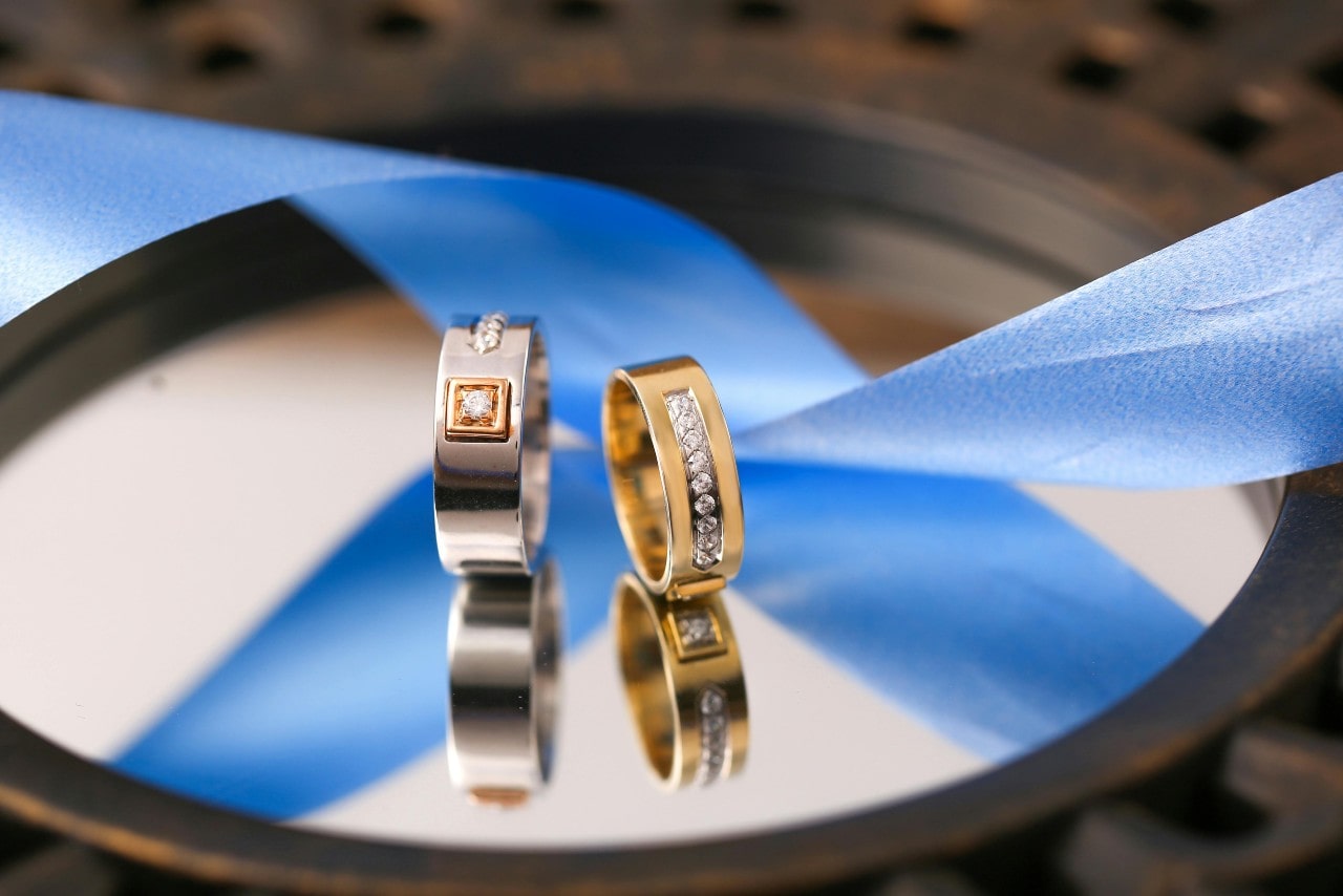 two mixed metal and diamond wedding bands sitting on a mirror next to a blue ribbon