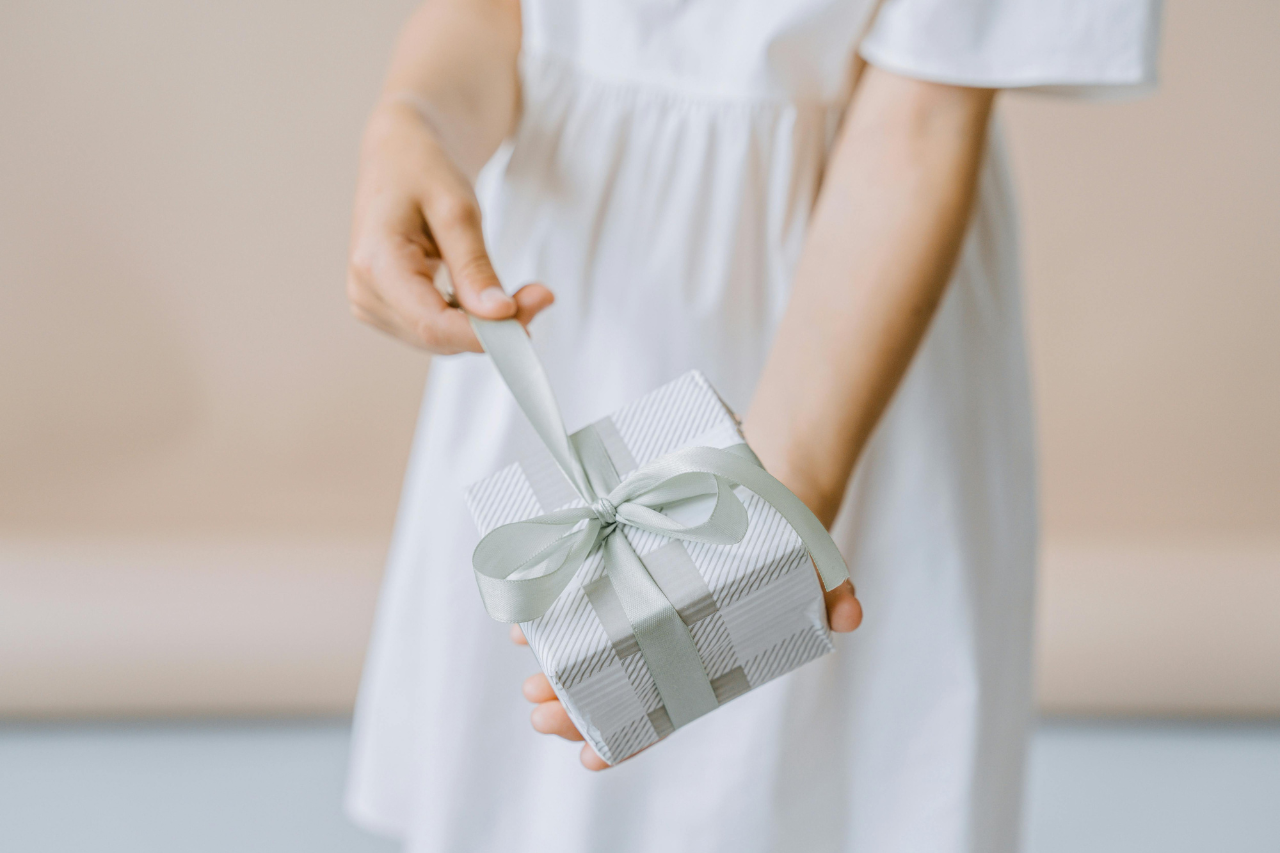 A close-up of a young woman dressed in white opening an elegantly wrapped gift.