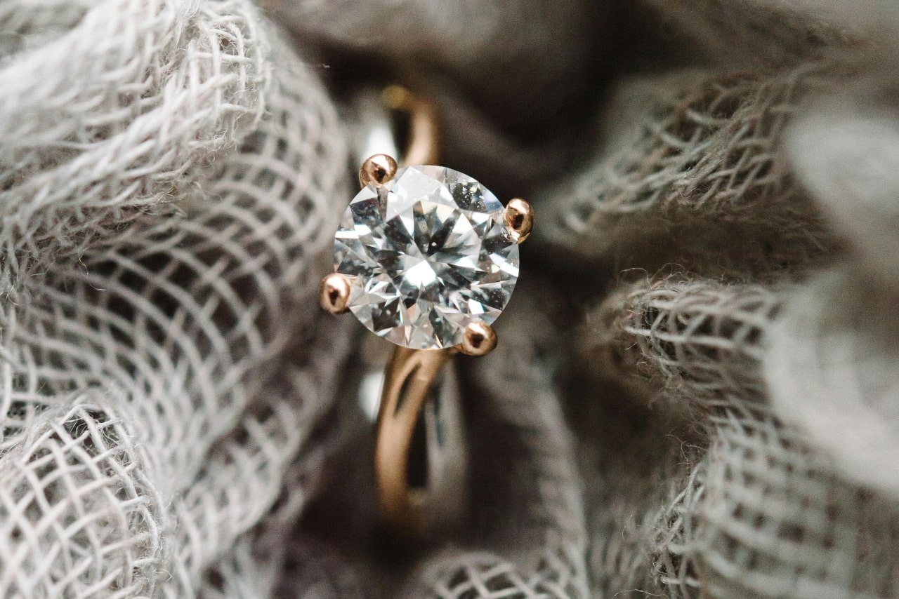 A close-up of a delicate mixed metal solitaire engagement ring wrapped in burlap.