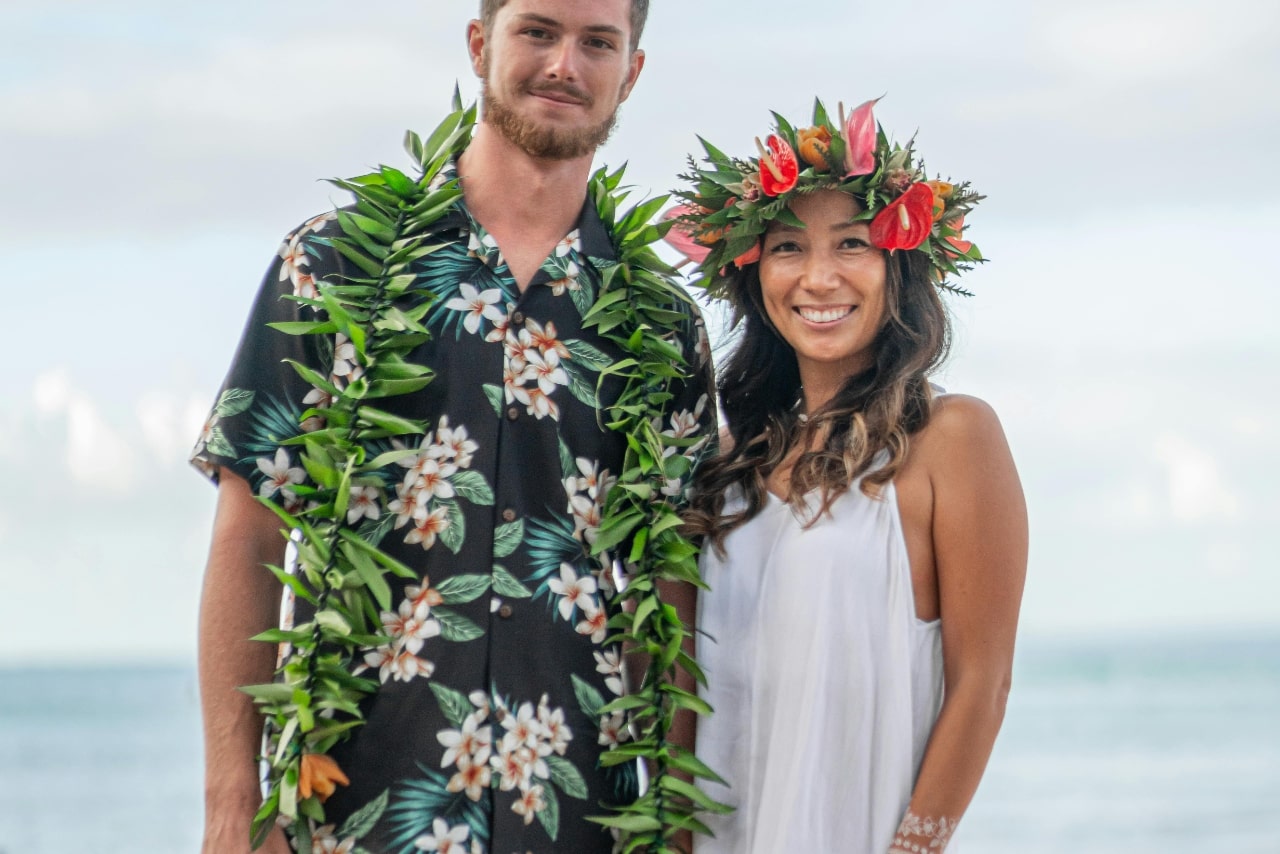 A casual photo of a newly engaged couple on the beach, the man wearing a ti leaf lei and the woman wearing a haku lei.