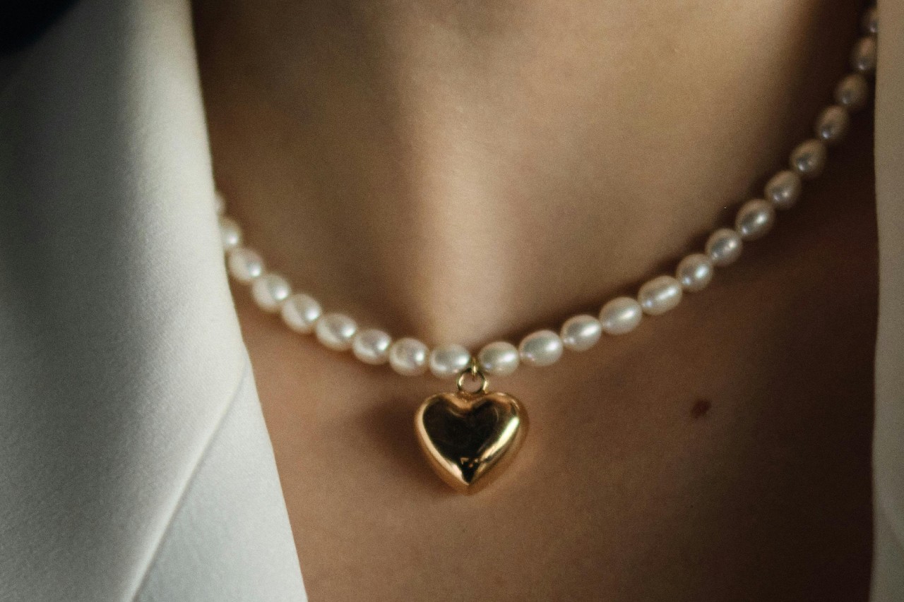 close up image of a woman’s neckline adorned with a pearl and heart pendant necklace