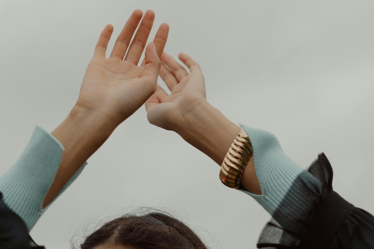 a woman’s hands raised above her head, wearing a bold gold bangle bracelet