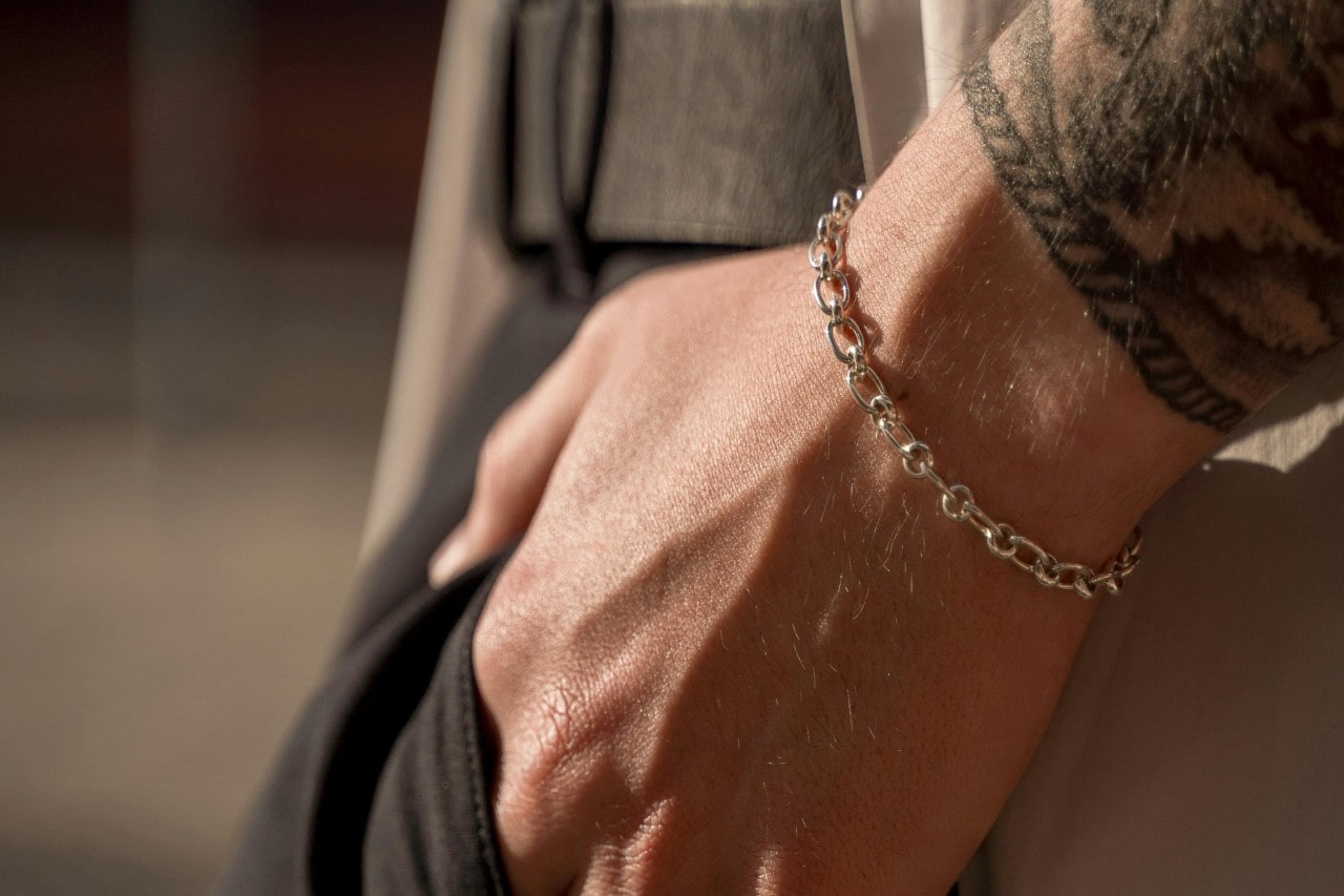 a man’s hand in his trousers pocket, wearing a white gold chain bracelet