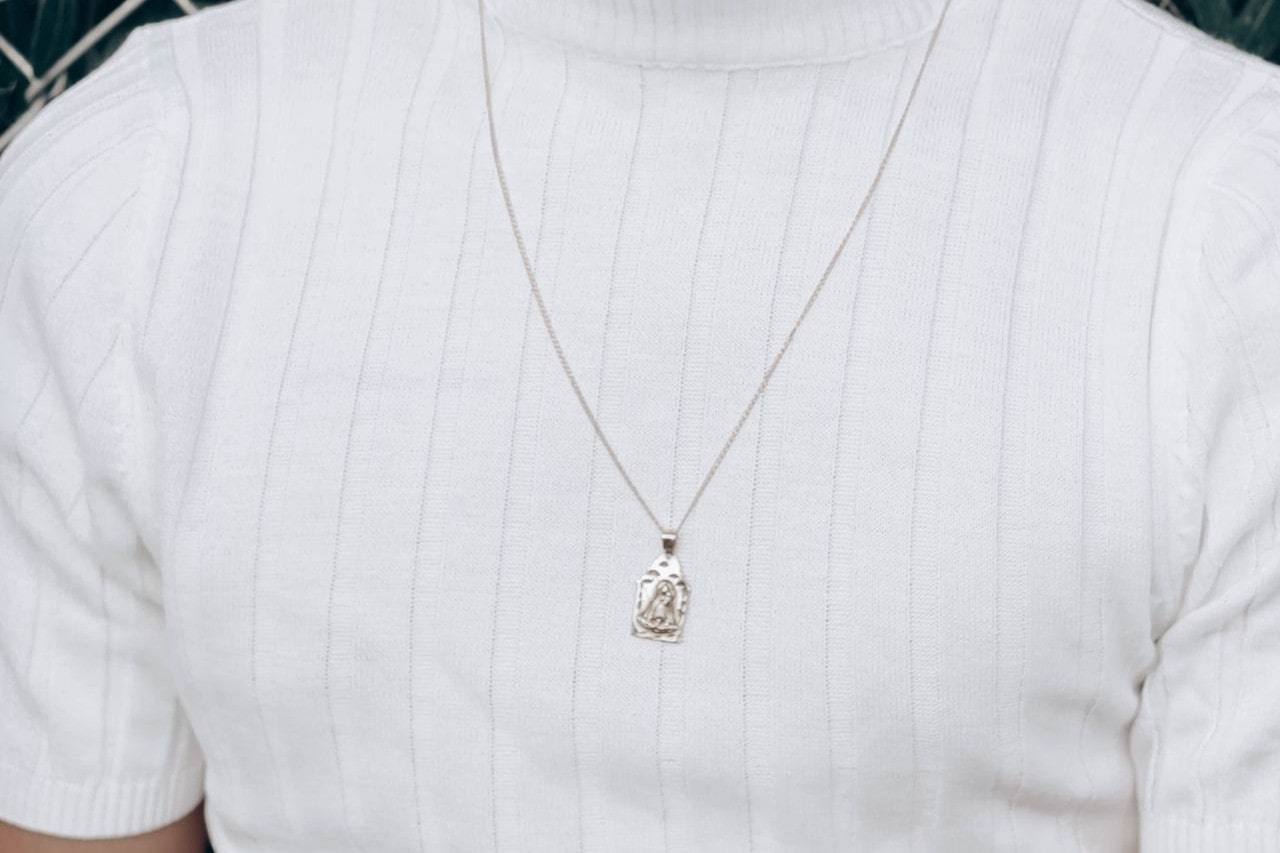 close up image of a man wearing a white striped shirt and a silver pendant necklace