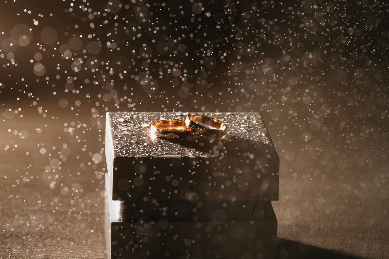 A spectacular shot of two rose gold wedding bands displayed atop a gift box, all beneath a rain of light and sparkles.