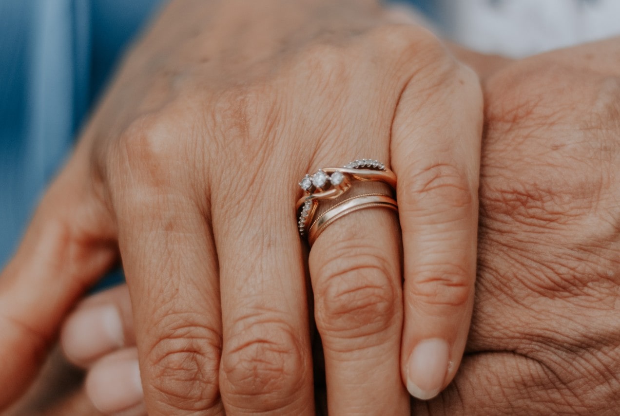 A close-up of a woman’s hand atop her husband’s, her ring finger adorned with a delicate rose gold bridal stack.