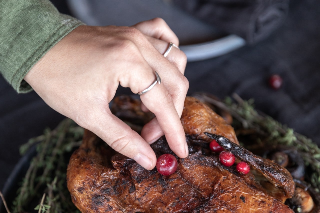 A close-up of a woman’s hand placing a cranberry on a thanksgiving turkey.