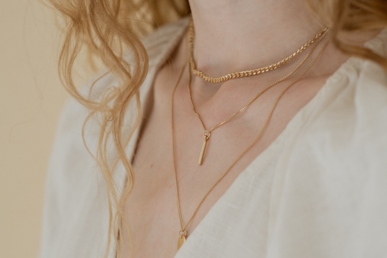 a woman wearing three layered yellow gold necklaces