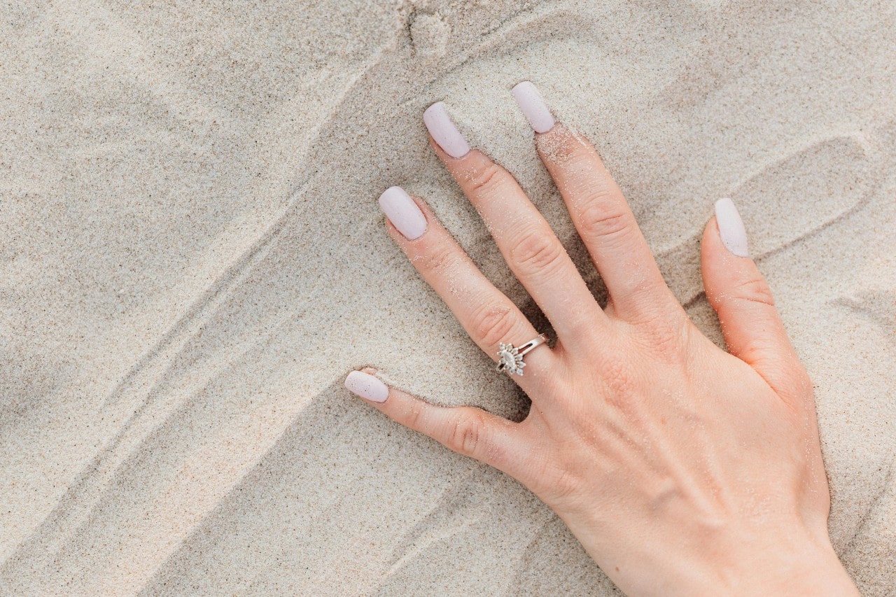 a woman’s hand in the sand wearing a white gold engagement ring