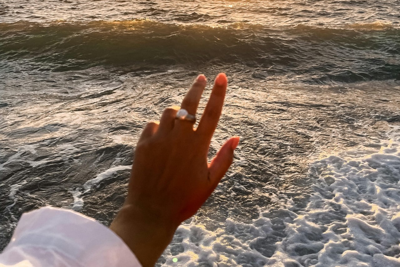 a woman’s hand outstretched towards the ocean, wearing a gold gemstone fashion ring