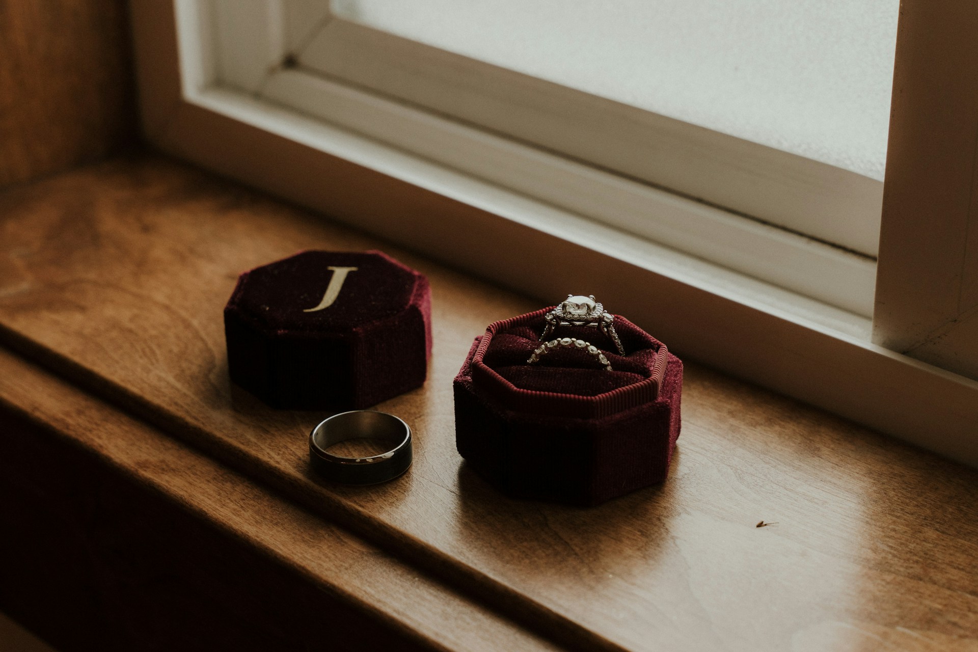 a black wedding band sitting on a windowsill next to other bridal rings