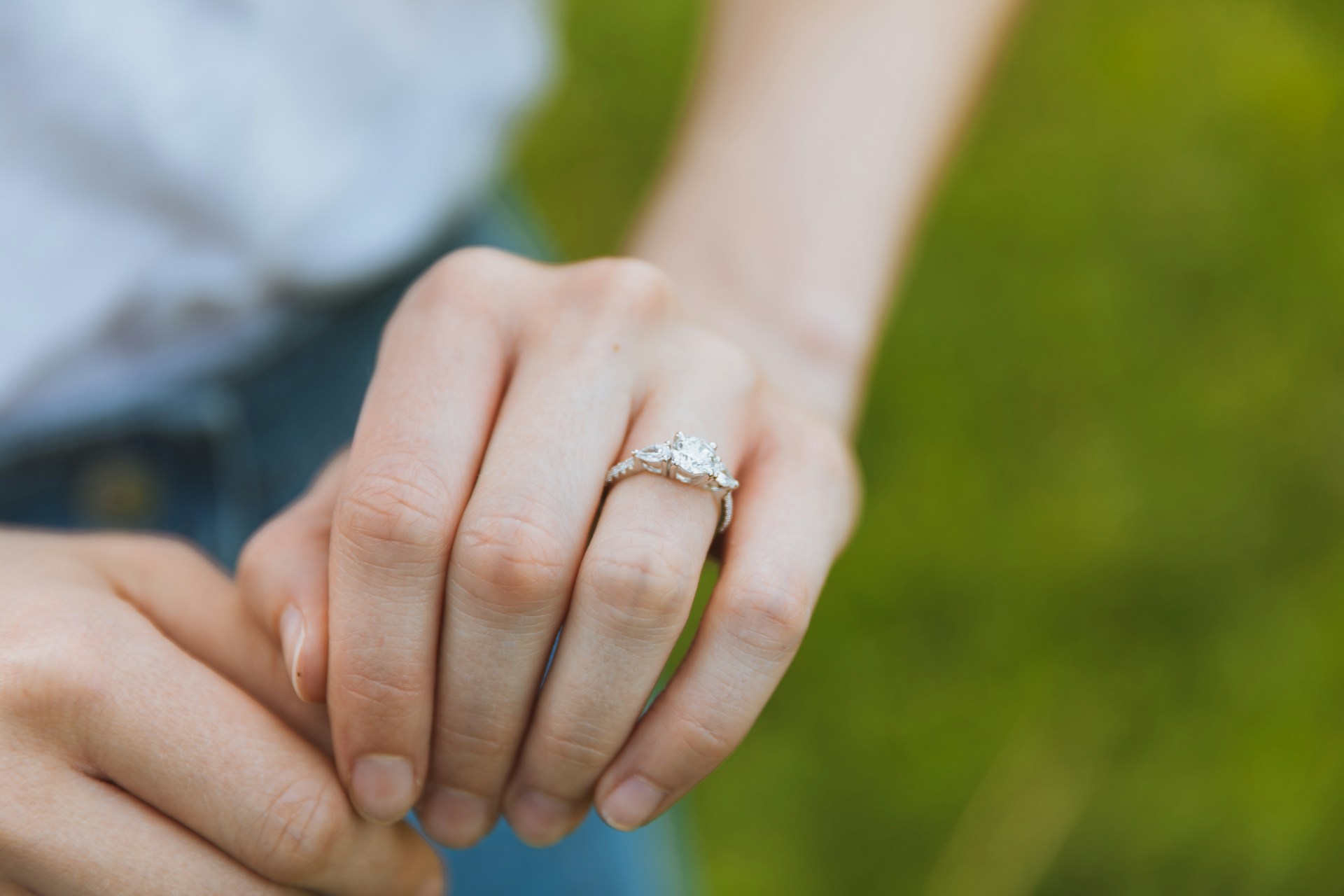 A close-up image of a woman’s hand adorned with a three stone engagement ring.