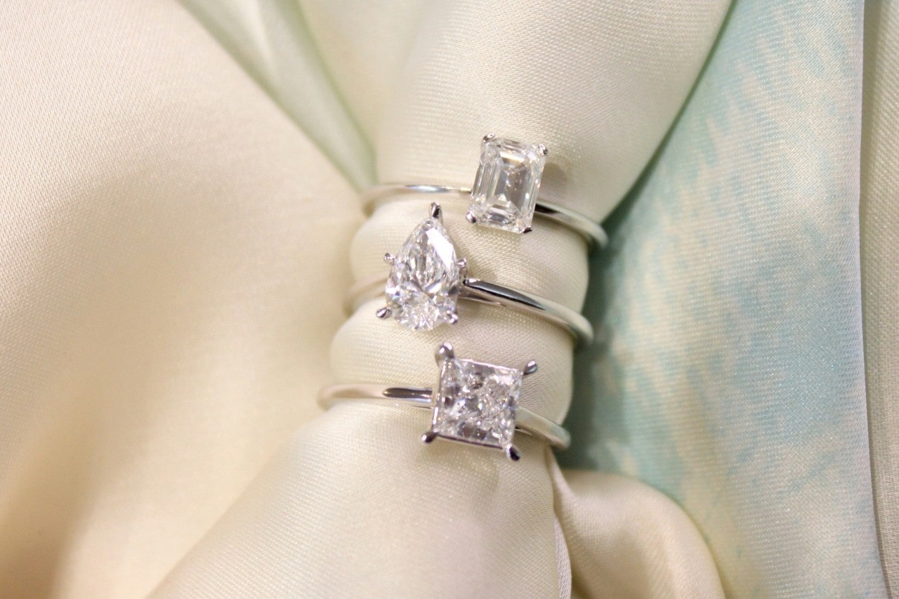 Three solitaire engagement rings stacked on a piece of white fabric.