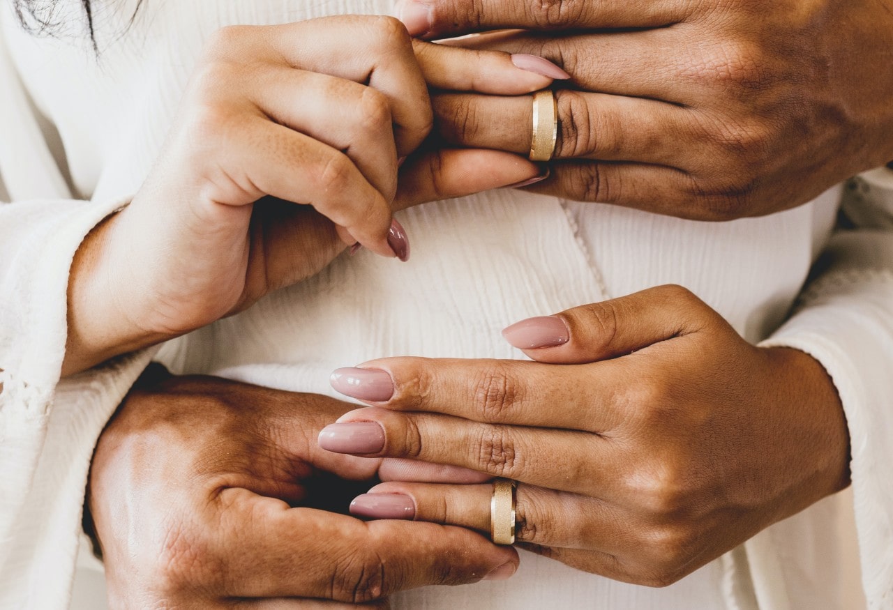 A woman and man simultaneously placing matching wide wedding bands on each other's fingers.