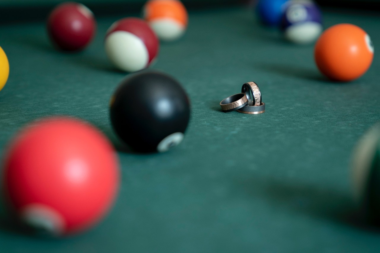 Three different colored wedding bands sitting on a pool table, stacked together.