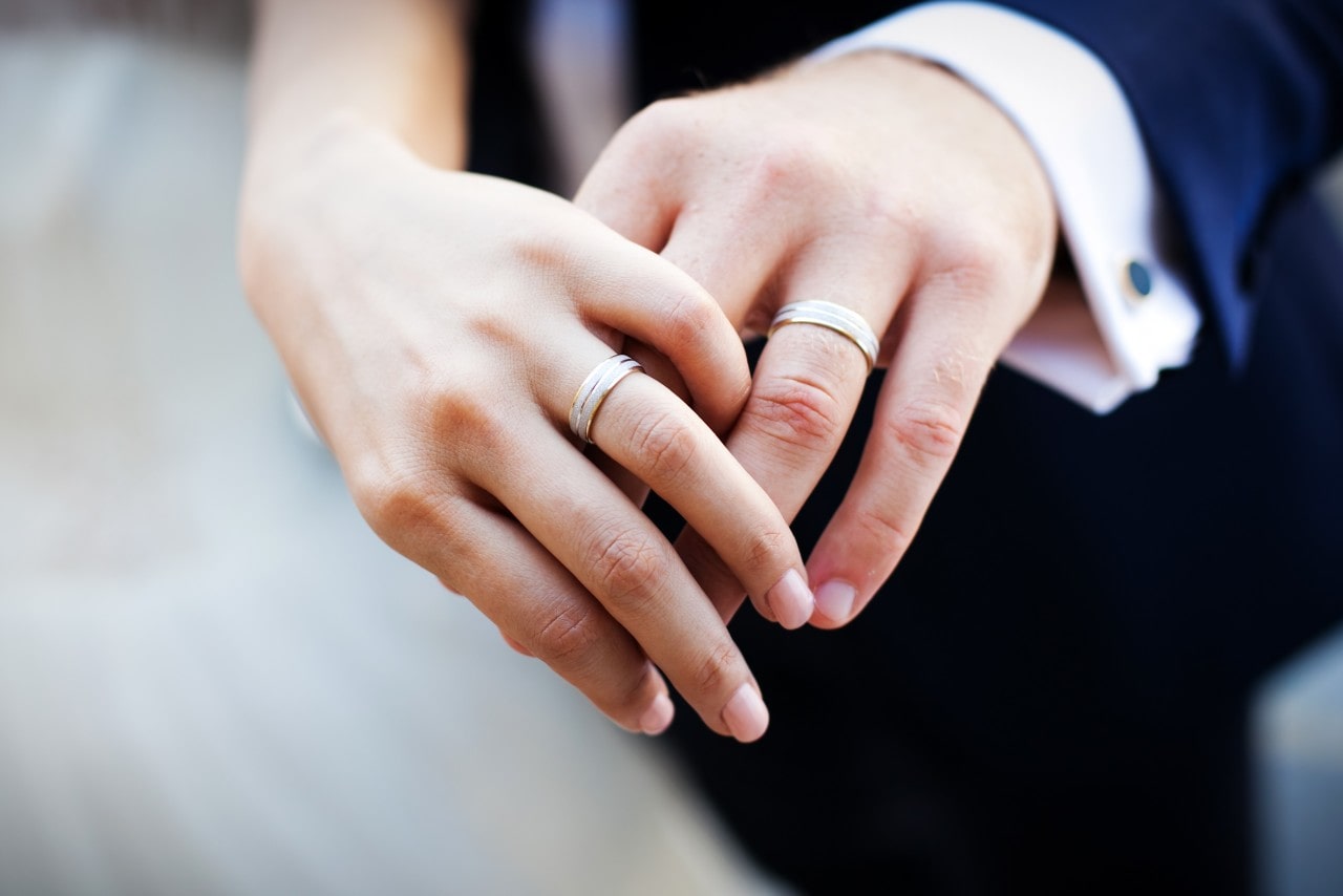 A bride and groom showing off their matching, wide wedding bands.